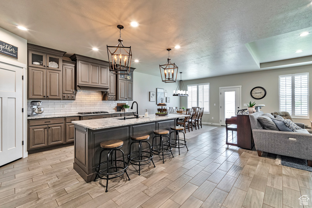 Kitchen with an island with sink, premium range hood, hanging light fixtures, stainless steel gas cooktop, and a kitchen bar