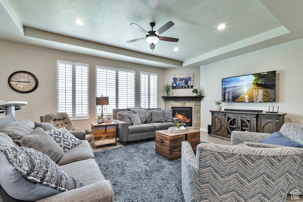 Living room featuring a stone fireplace, ceiling fan, and a tray ceiling