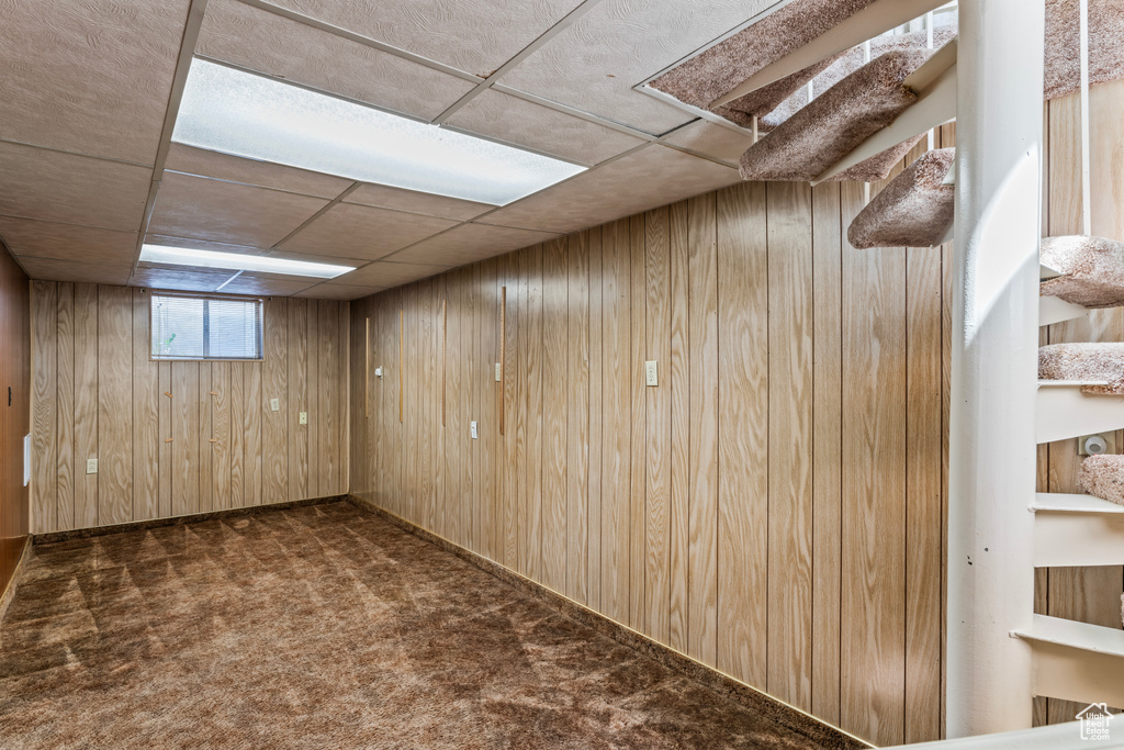 Basement featuring wooden walls, dark carpet, and a paneled ceiling
