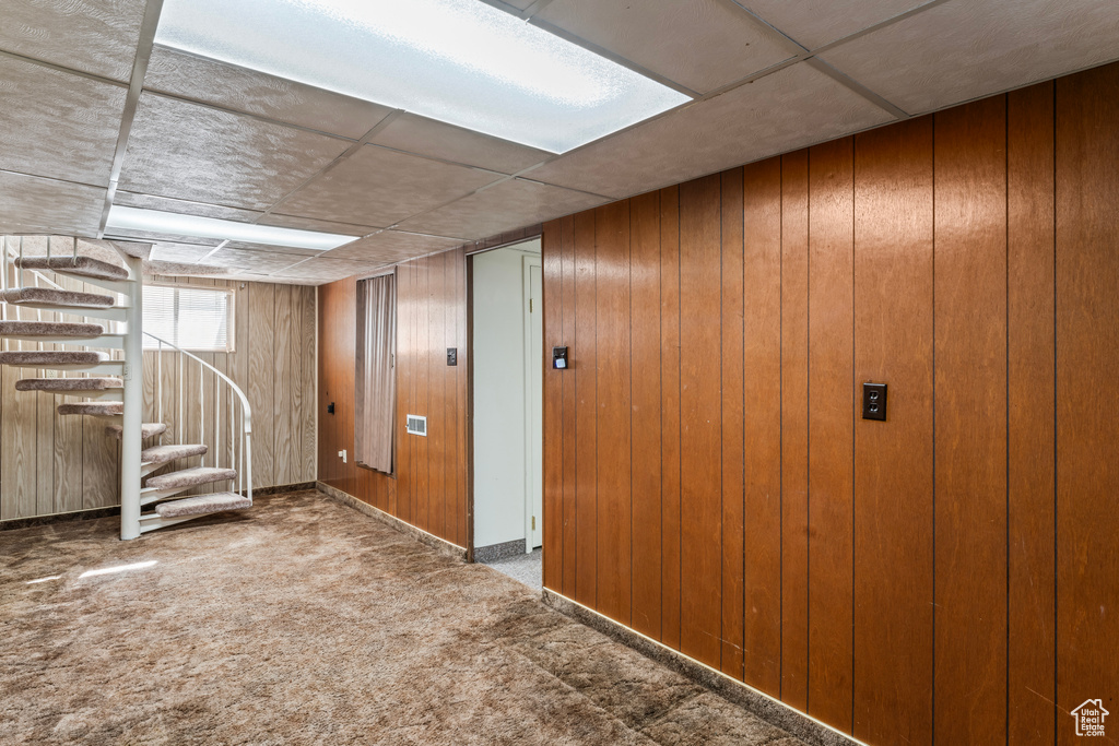 Basement featuring carpet floors, wood walls, elevator, and a drop ceiling