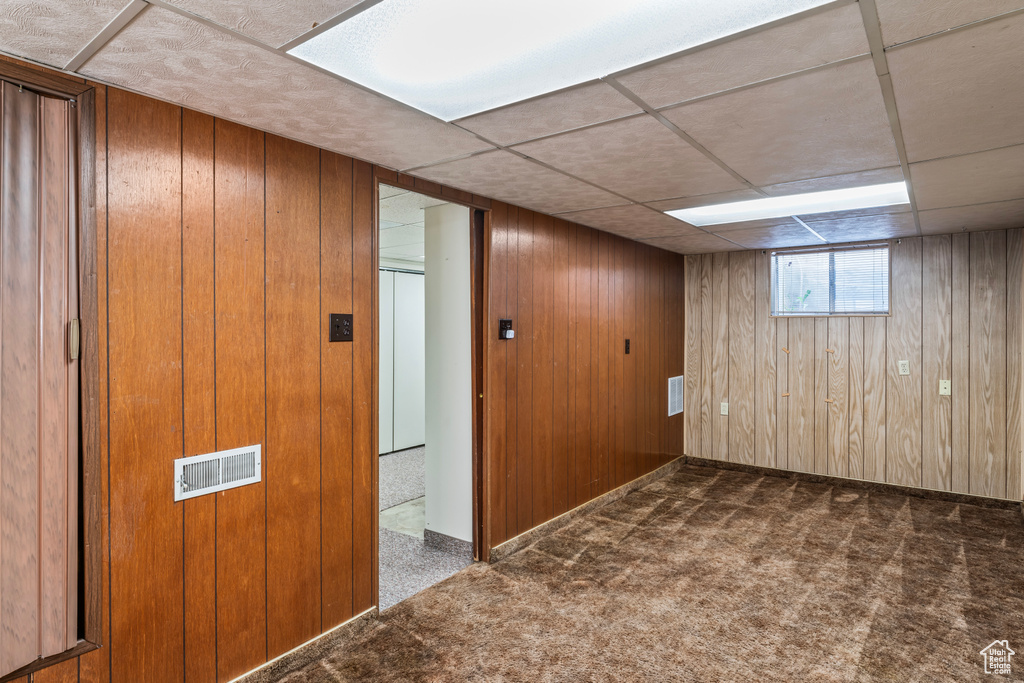 Basement with wooden walls, carpet floors, and a paneled ceiling