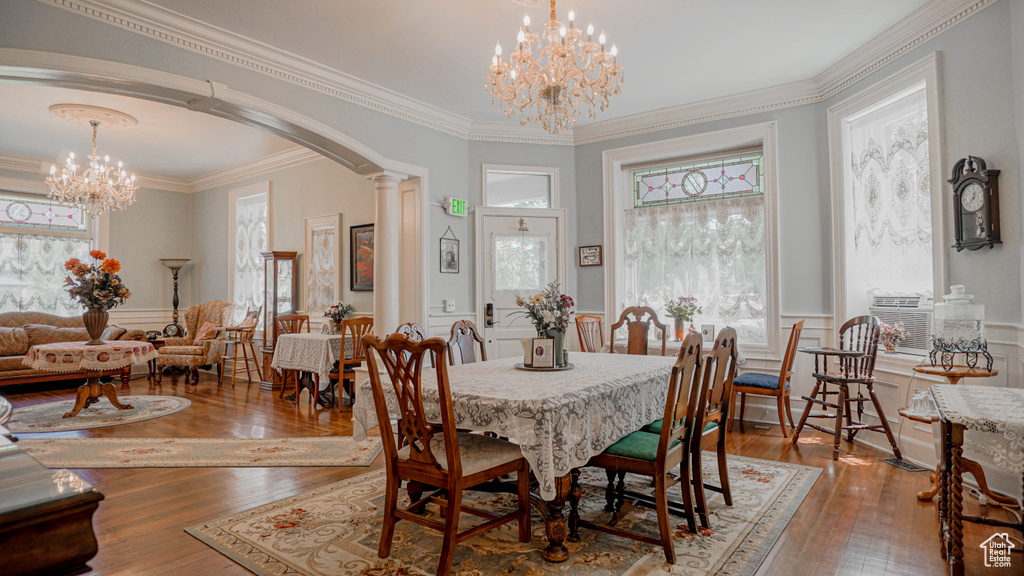 Dining room with crown molding, decorative columns, a notable chandelier, and hardwood / wood-style floors