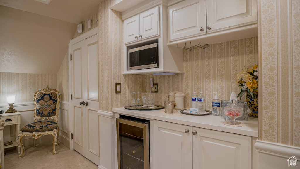 Kitchen with stainless steel microwave, beverage cooler, light colored carpet, and white cabinetry