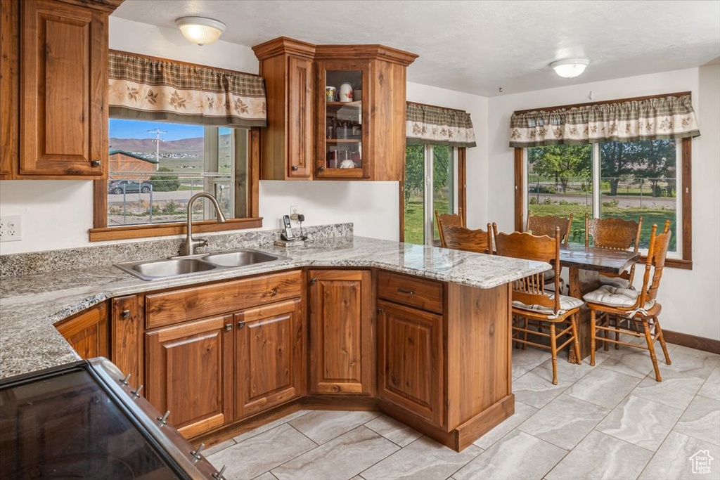 Kitchen with light stone counters, sink, light tile floors, and kitchen peninsula