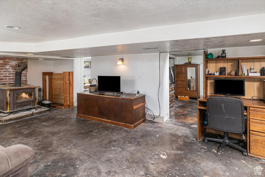 Office featuring brick wall, concrete floors, a wood stove, and a textured ceiling