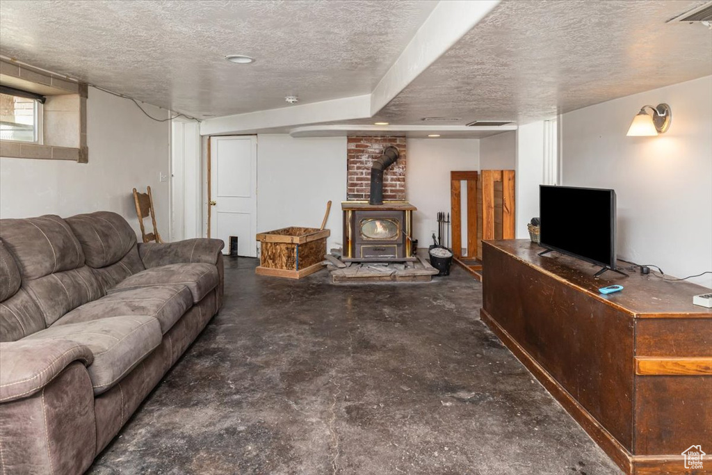 Living room featuring concrete flooring, a textured ceiling, a wood stove, and brick wall