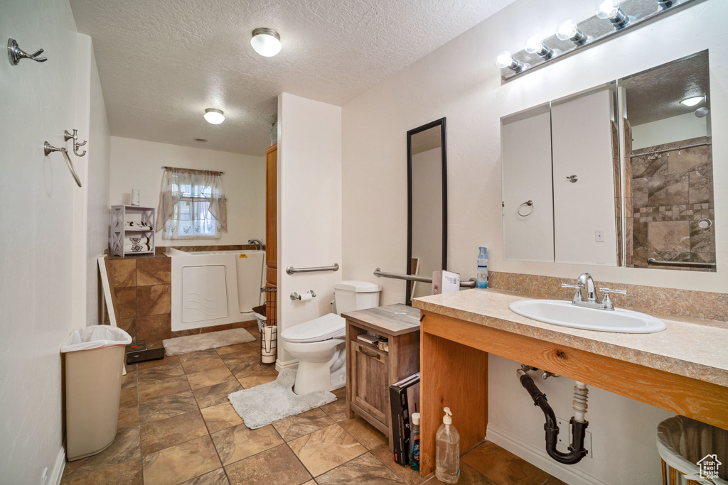 Bathroom with tile floors, vanity with extensive cabinet space, a textured ceiling, and toilet