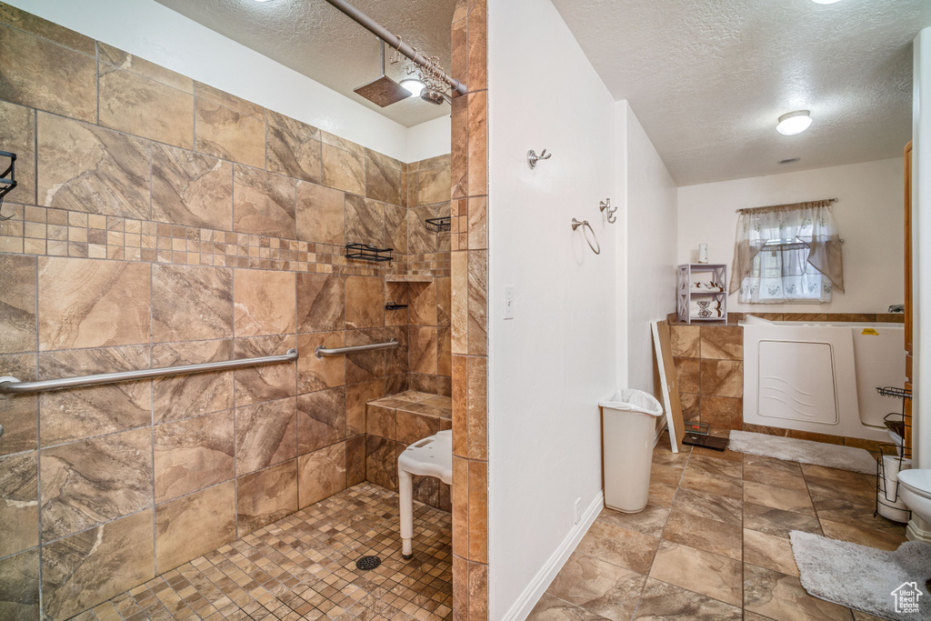 Bathroom featuring a tile shower, a textured ceiling, toilet, and tile floors