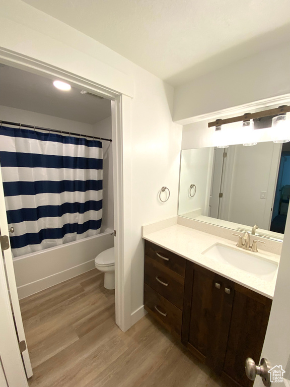 Full bathroom with wood-type flooring, shower / bath combo with shower curtain, vanity, and toilet