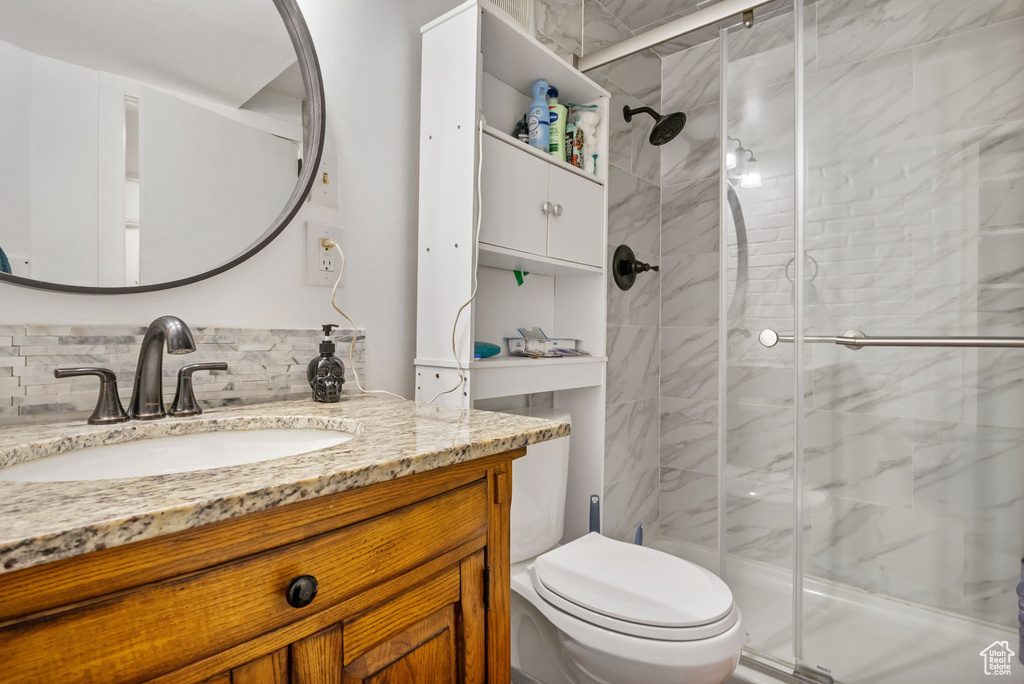 Bathroom featuring backsplash, vanity, toilet, and a shower with door