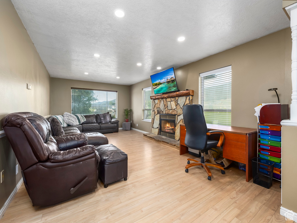 Office space with a stone fireplace, light hardwood / wood-style floors, and a textured ceiling