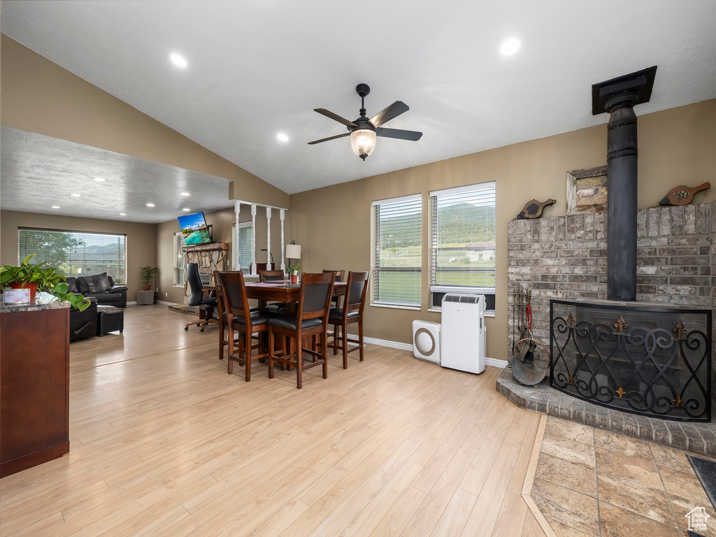 Dining room featuring vaulted ceiling, ceiling fan, a wood stove, and light hardwood / wood-style flooring