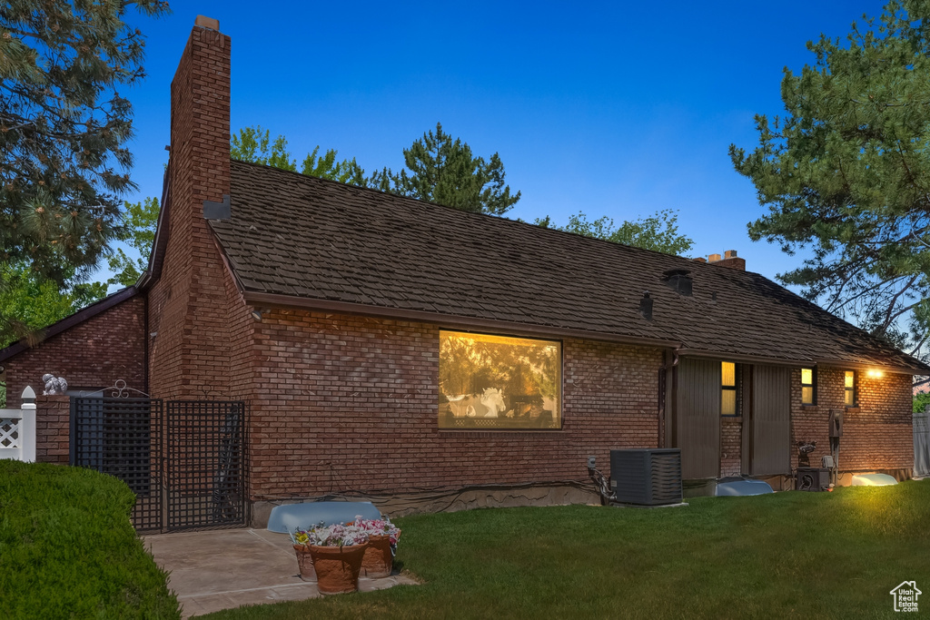 Back house at dusk with a yard, a patio, and central air condition unit