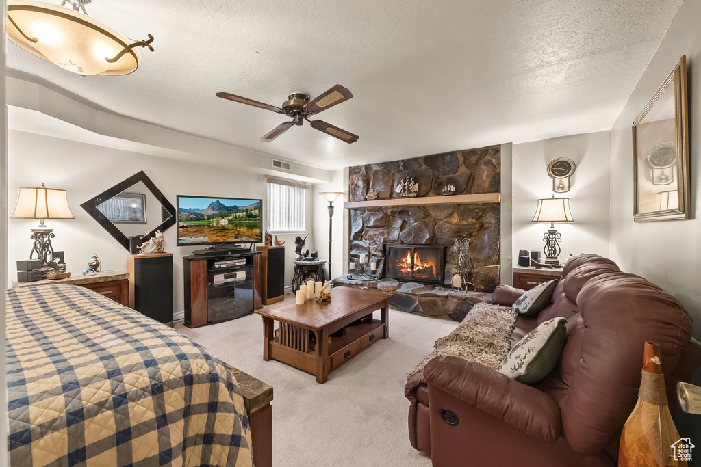 Carpeted bedroom with a textured ceiling, a stone fireplace, and ceiling fan