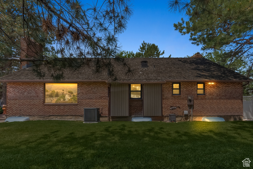 Back house at dusk with central AC unit and a yard