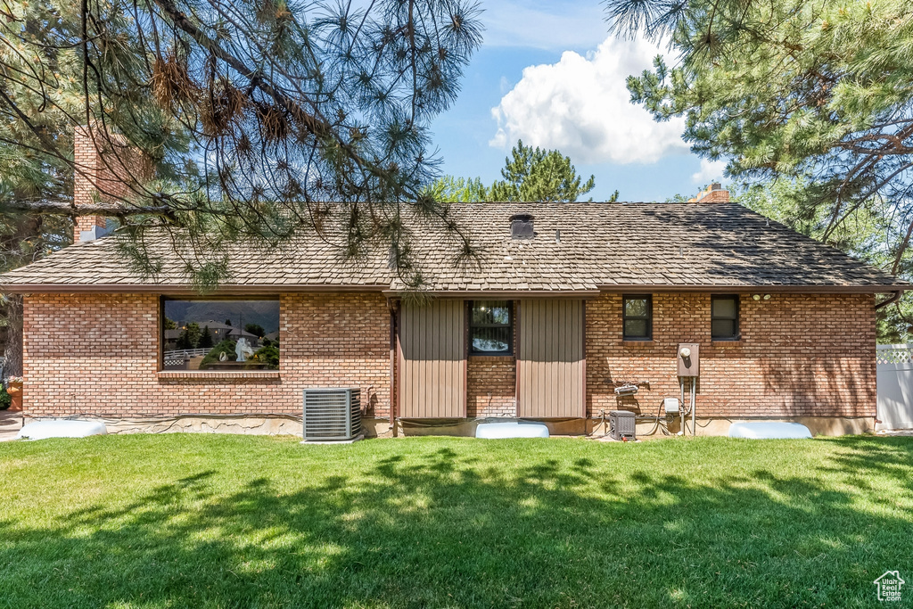 Back of house with a yard and central AC