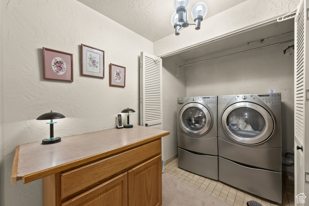 Washroom featuring a chandelier, light tile patterned floors, washer and dryer, and a textured ceiling