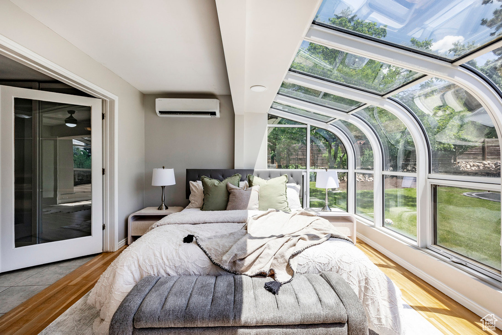 Bedroom featuring an AC wall unit, multiple windows, and hardwood / wood-style floors