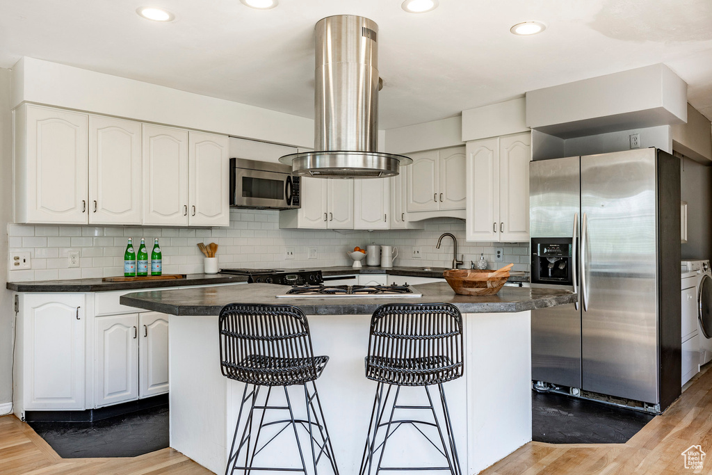 Kitchen featuring a kitchen island, stainless steel appliances, tasteful backsplash, light wood-type flooring, and white cabinets