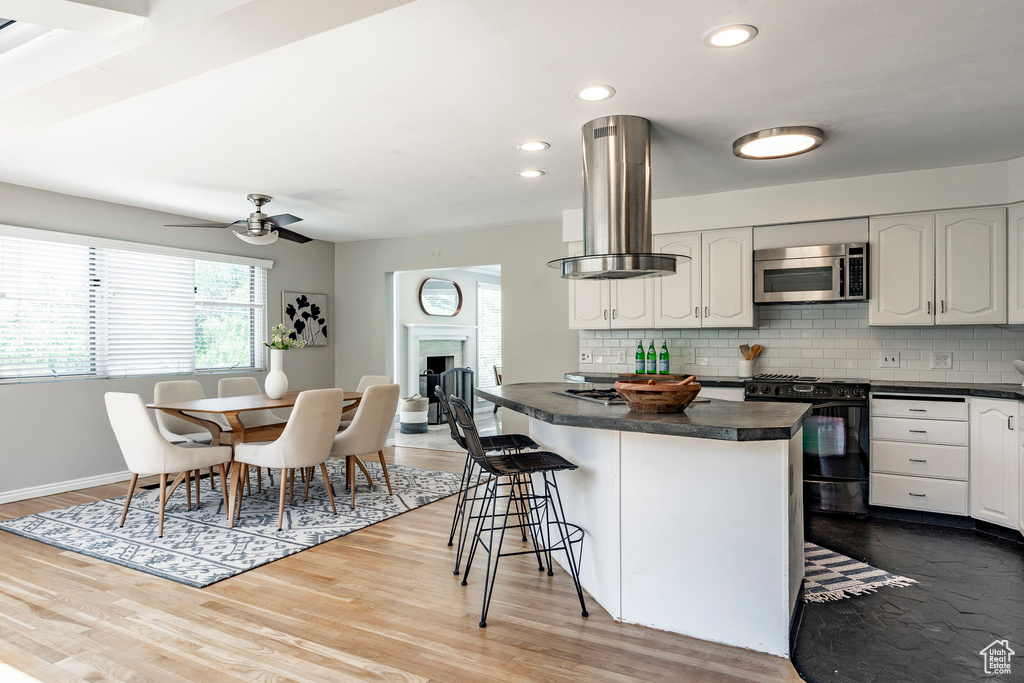 Kitchen featuring black stove, light hardwood / wood-style flooring, tasteful backsplash, island range hood, and white cabinets