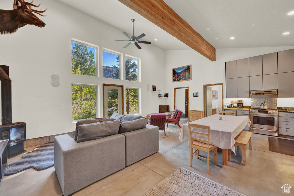 Living room featuring beamed ceiling, high vaulted ceiling, ceiling fan, and a wood stove