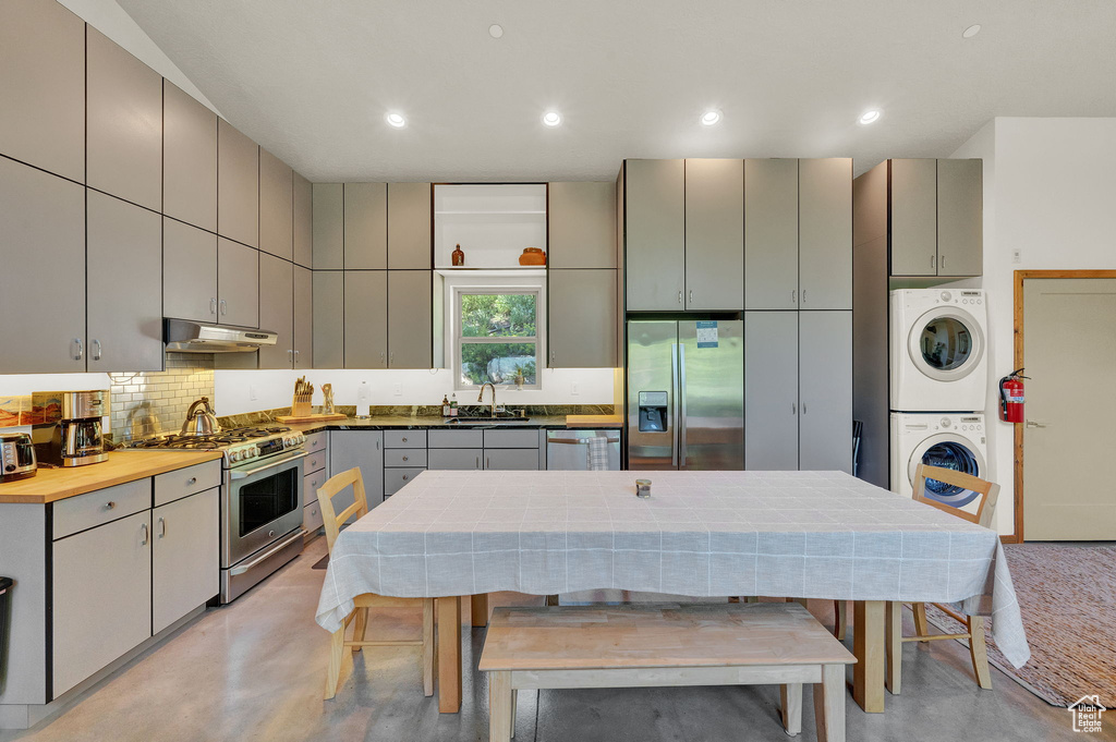 Kitchen with stainless steel appliances, gray cabinets, stacked washer / drying machine, backsplash, and sink