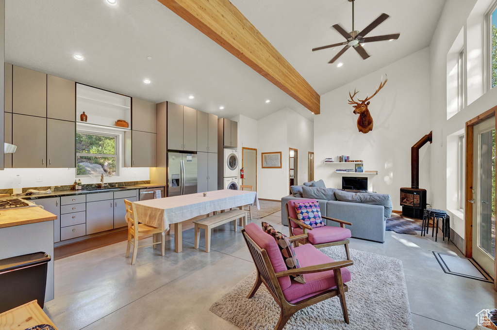 Living room with a wood stove, ceiling fan, beam ceiling, high vaulted ceiling, and stacked washing maching and dryer