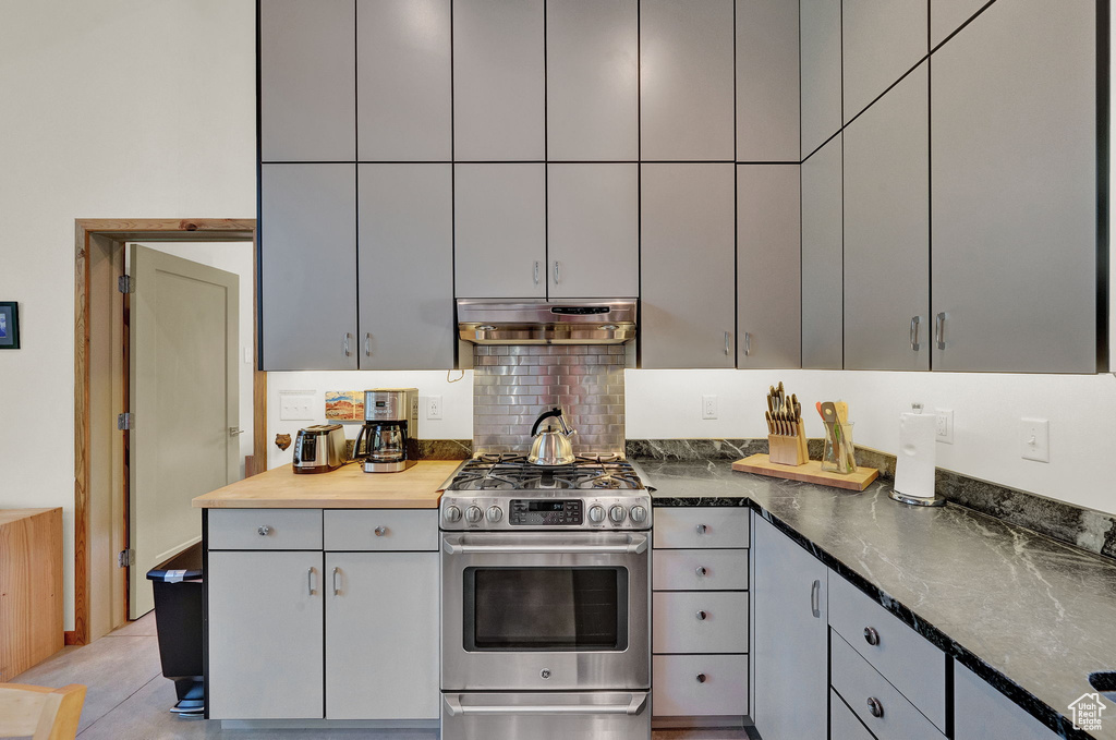 Kitchen featuring range hood, gray cabinetry, stainless steel gas stove, tasteful backsplash, and light tile flooring