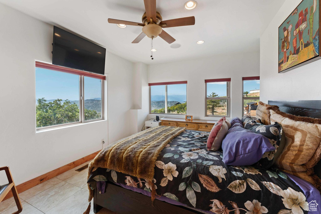 Tiled bedroom featuring multiple windows and ceiling fan