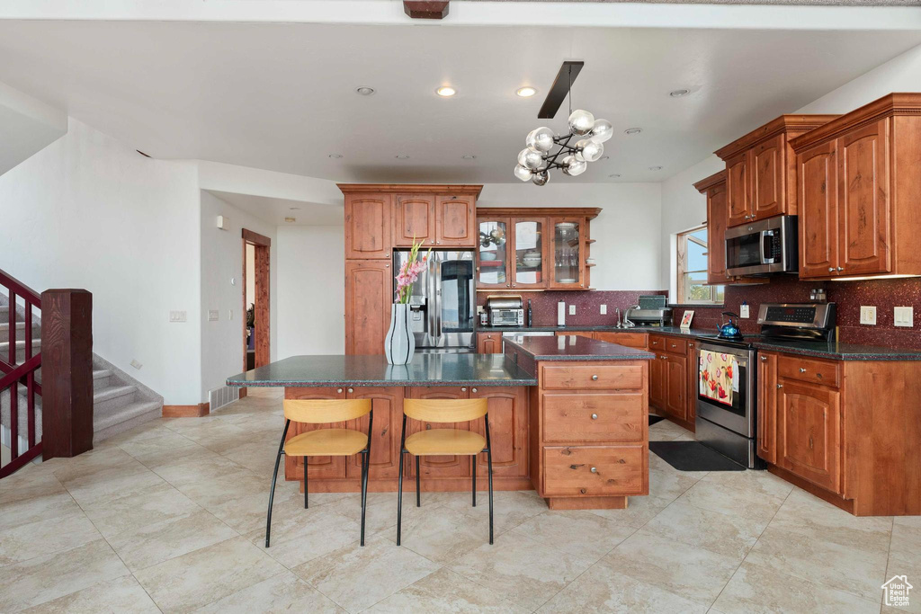 Kitchen featuring a center island, stainless steel appliances, a notable chandelier, and decorative backsplash