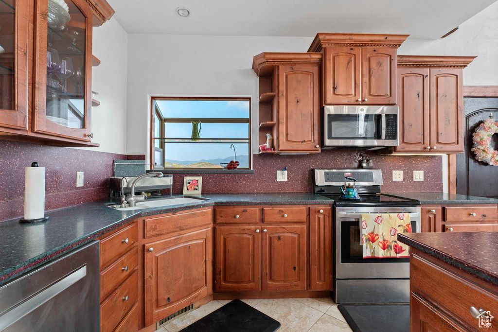 Kitchen with stainless steel appliances, sink, decorative backsplash, and light tile patterned flooring