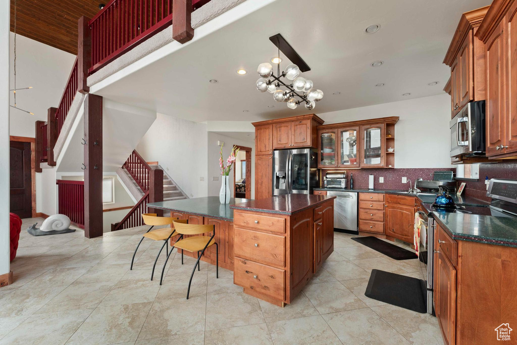 Kitchen with pendant lighting, a notable chandelier, appliances with stainless steel finishes, a center island, and decorative backsplash