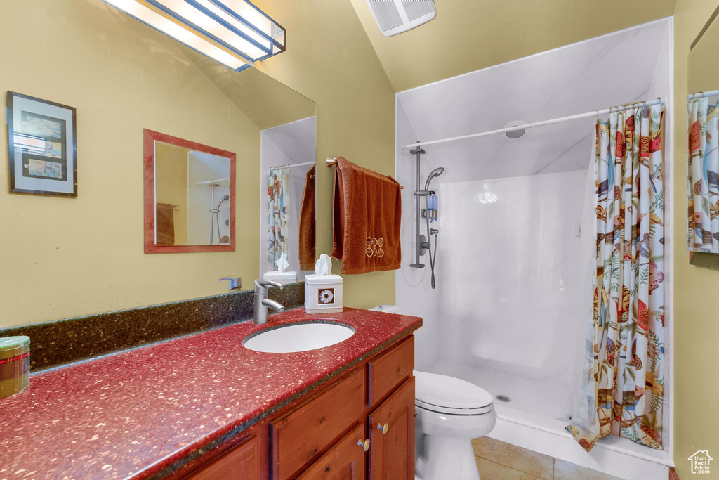 Bathroom featuring vaulted ceiling, vanity with extensive cabinet space, toilet, tile floors, and walk in shower