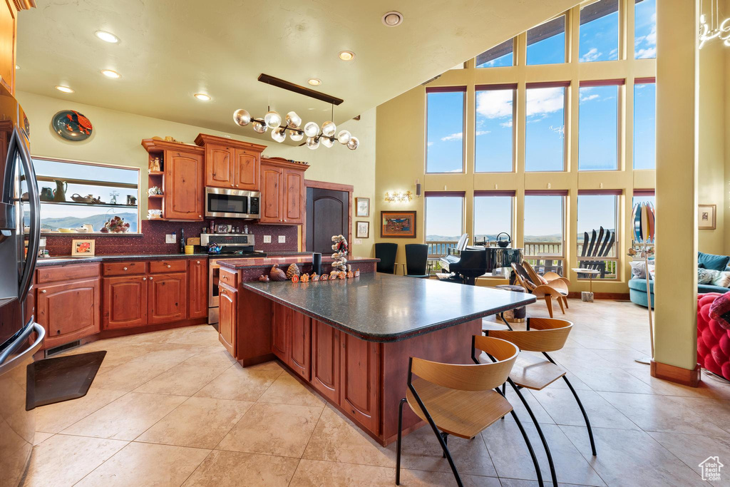 Kitchen featuring stainless steel appliances, a high ceiling, backsplash, pendant lighting, and light tile flooring