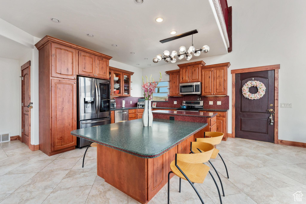 Kitchen with tasteful backsplash, stainless steel appliances, a kitchen breakfast bar, an inviting chandelier, and a center island