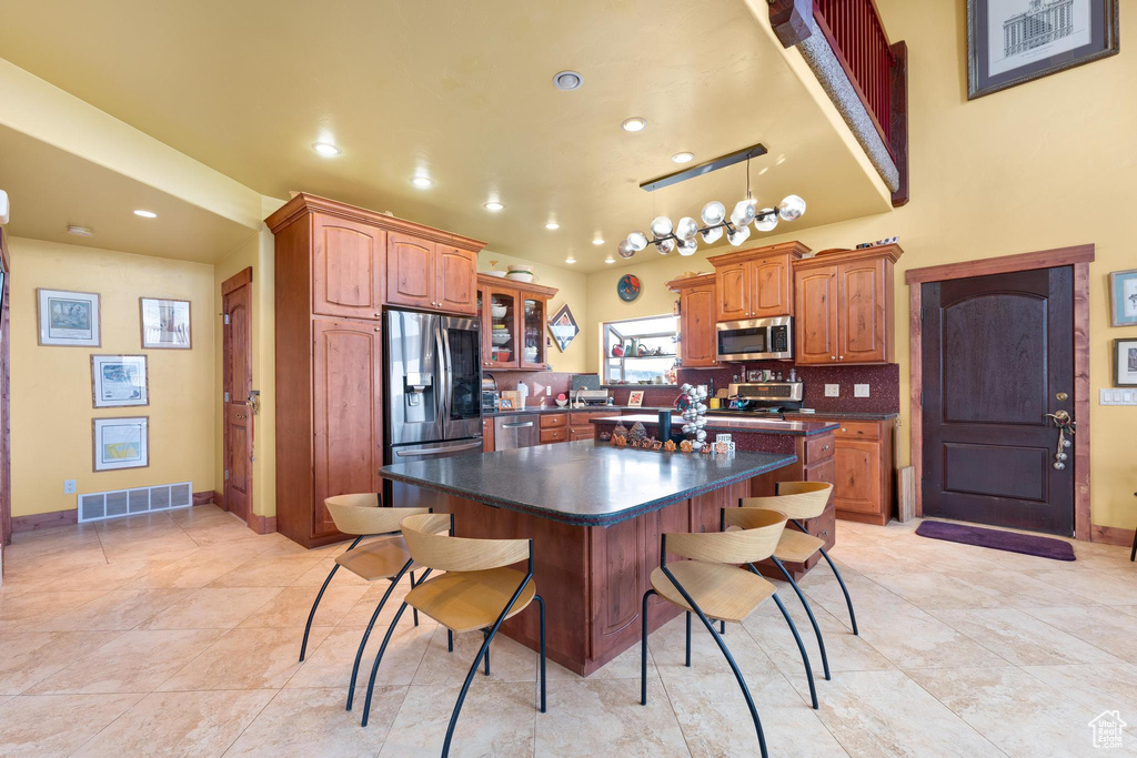 Kitchen featuring tasteful backsplash, light tile flooring, a kitchen island, a breakfast bar area, and appliances with stainless steel finishes