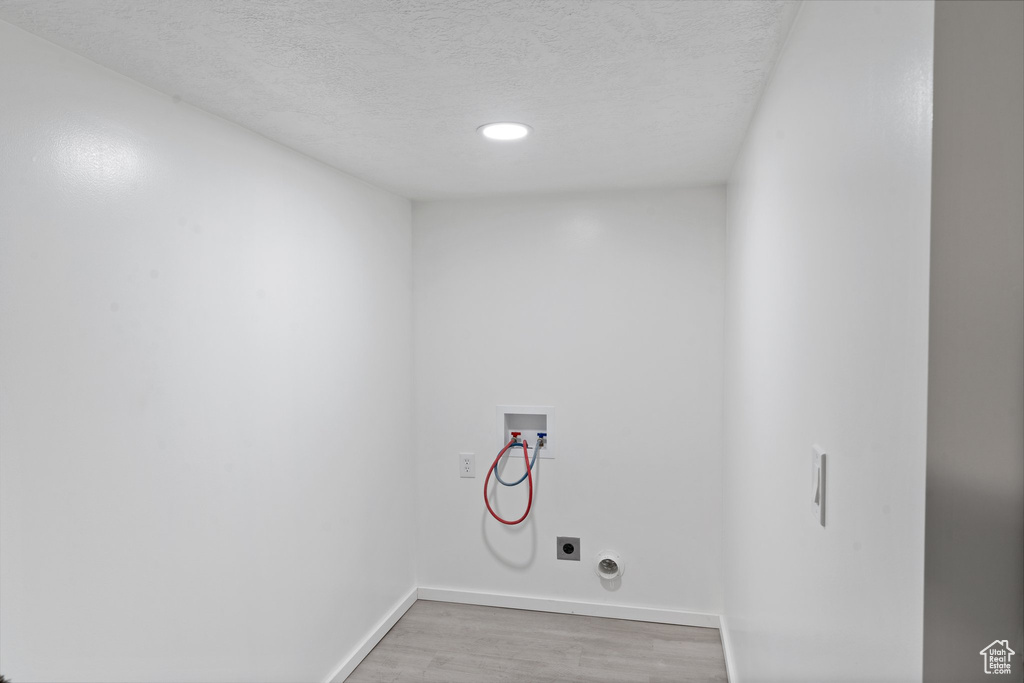 Clothes washing area with hookup for a washing machine, a textured ceiling, hookup for an electric dryer, and wood-type flooring