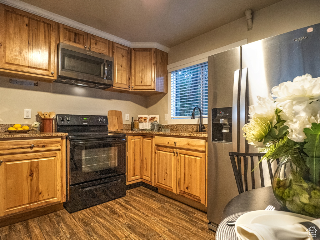 Kitchen featuring dark hardwood / wood-style floors, sink, appliances with stainless steel finishes, ornamental molding, and dark stone countertops