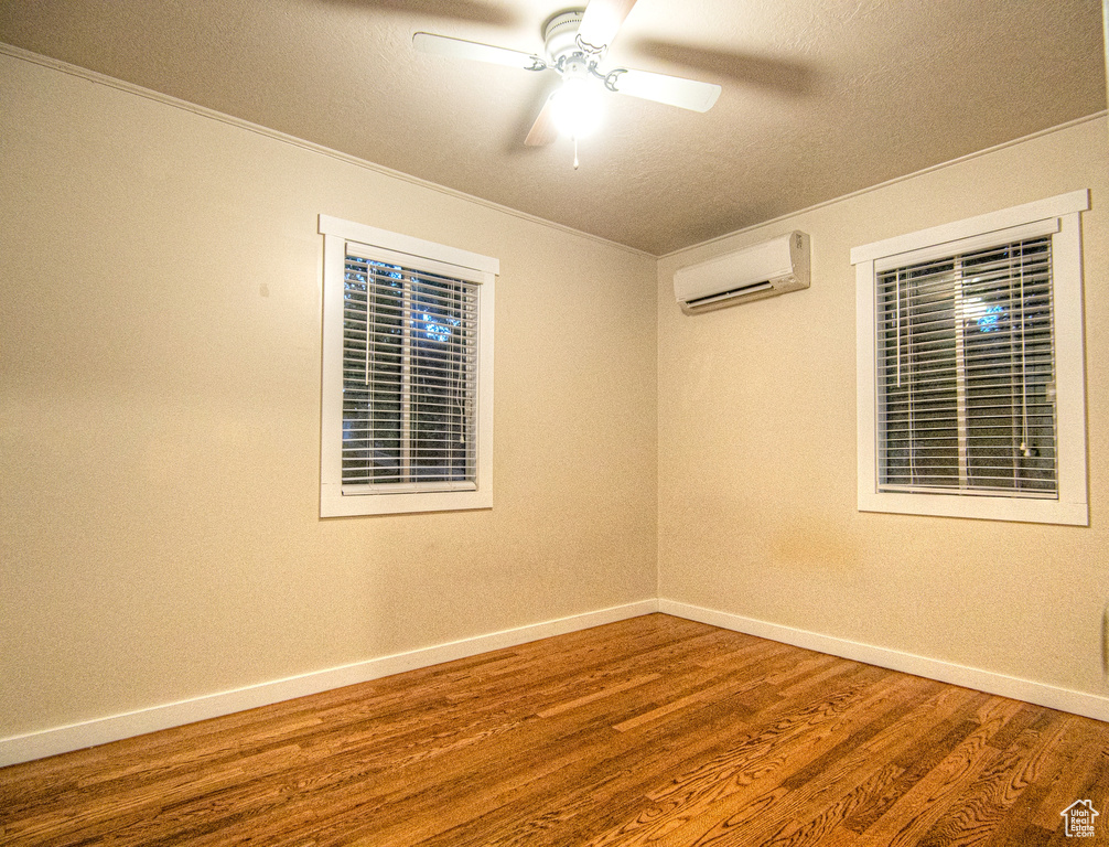 Empty room featuring ceiling fan, hardwood / wood-style flooring, a wall mounted air conditioner, and a textured ceiling