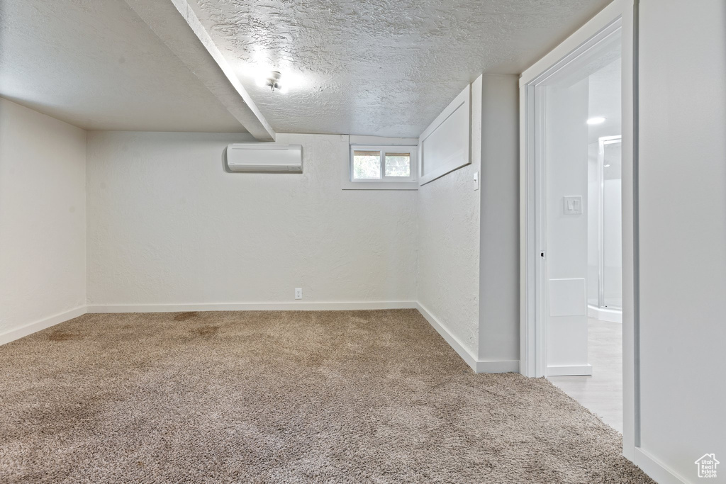 Basement featuring a wall unit AC, a textured ceiling, and carpet