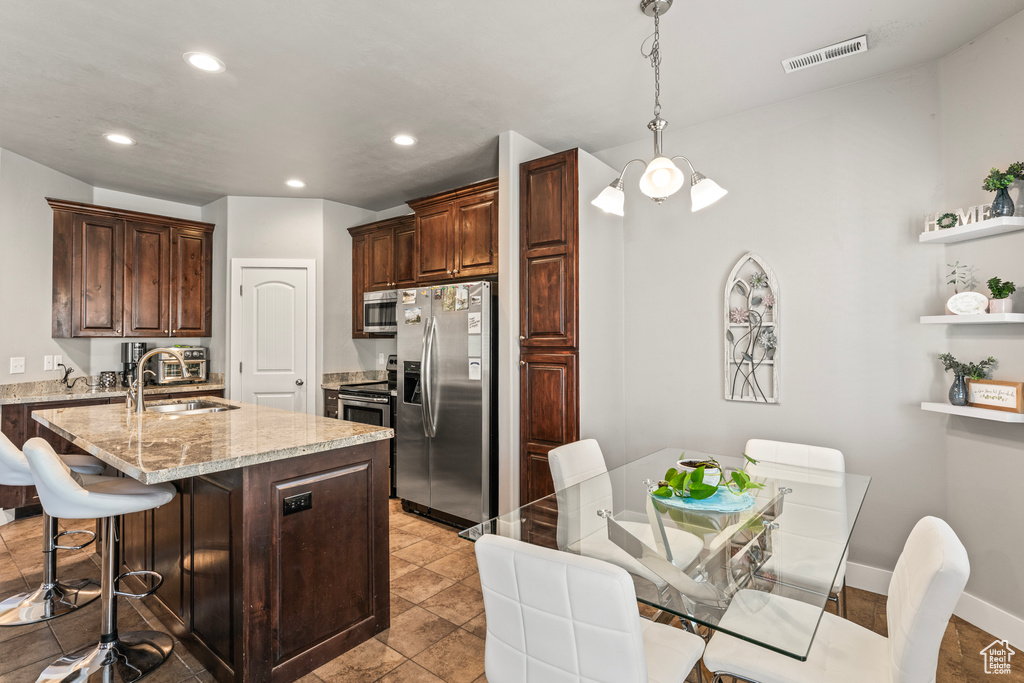 Kitchen featuring stainless steel appliances, decorative light fixtures, light tile flooring, sink, and a kitchen island with sink