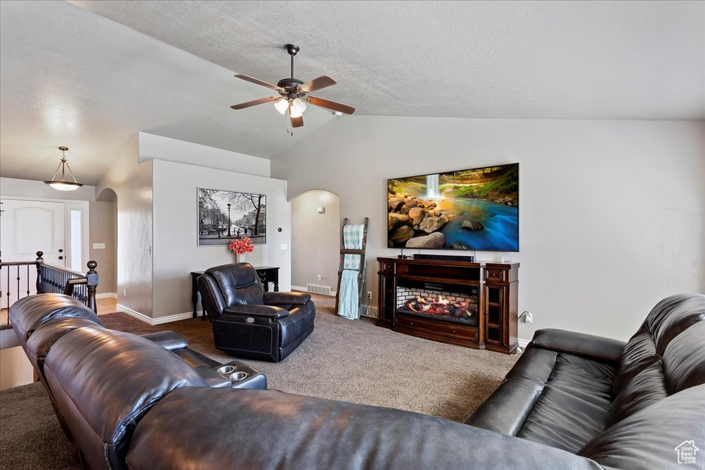 Carpeted living room featuring ceiling fan, a fireplace, and lofted ceiling