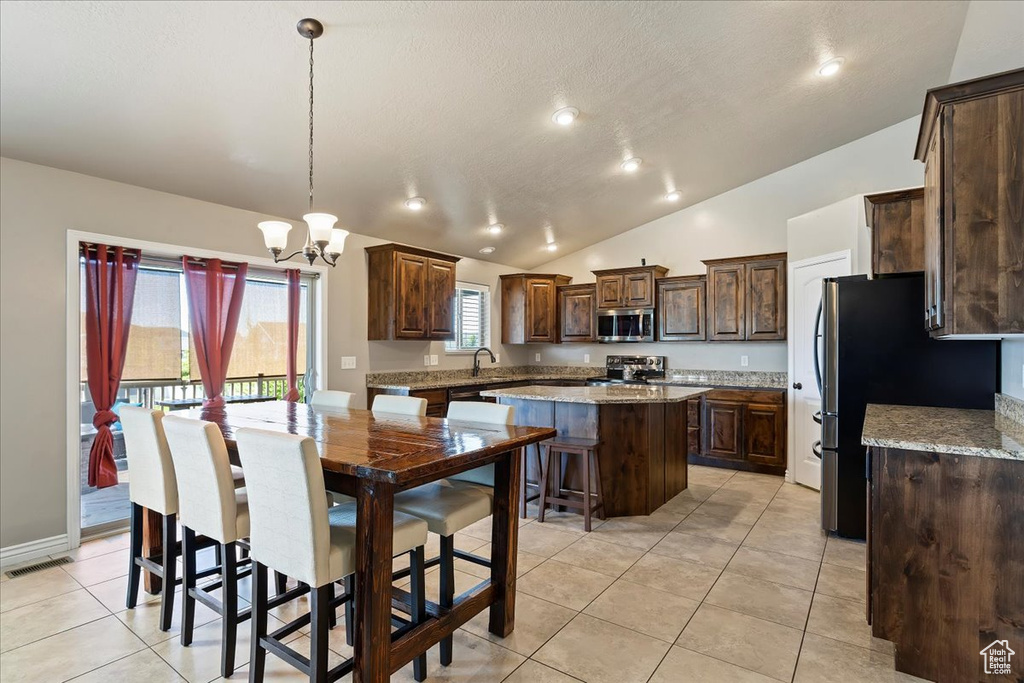 Kitchen with a center island, lofted ceiling, stove, pendant lighting, and light tile flooring