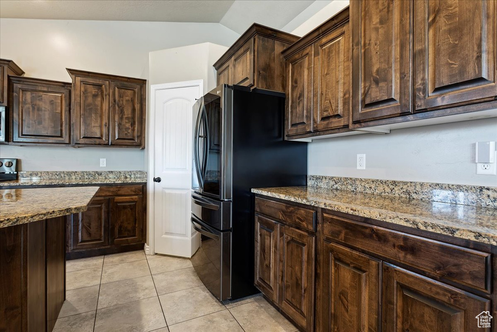 Kitchen featuring light tile flooring, dark brown cabinets, vaulted ceiling, and black refrigerator