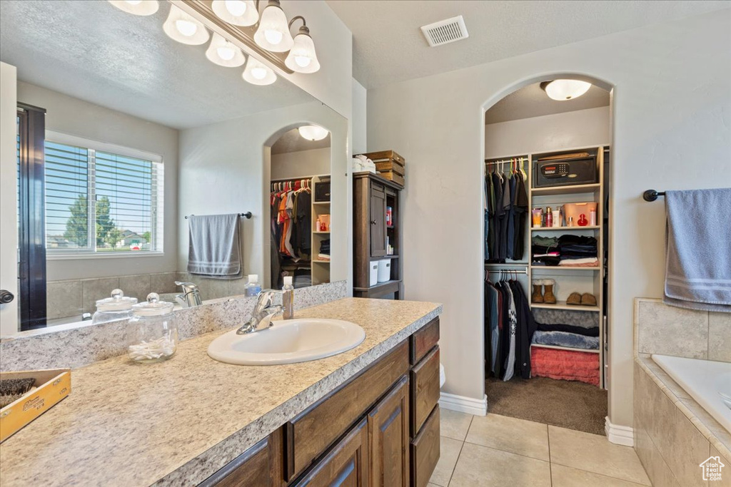 Bathroom with tile flooring, tiled bath, oversized vanity, and a textured ceiling