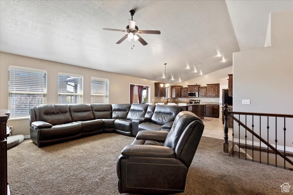 Living room with a textured ceiling, lofted ceiling, ceiling fan, and light colored carpet