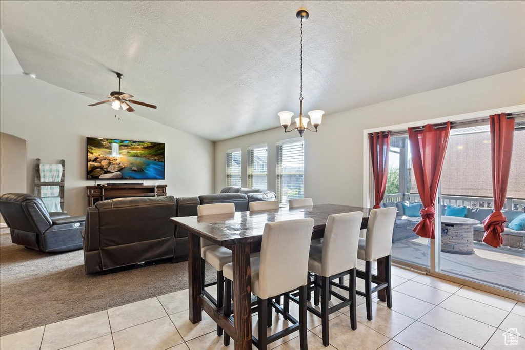 Tiled dining area featuring a textured ceiling, lofted ceiling, and ceiling fan with notable chandelier