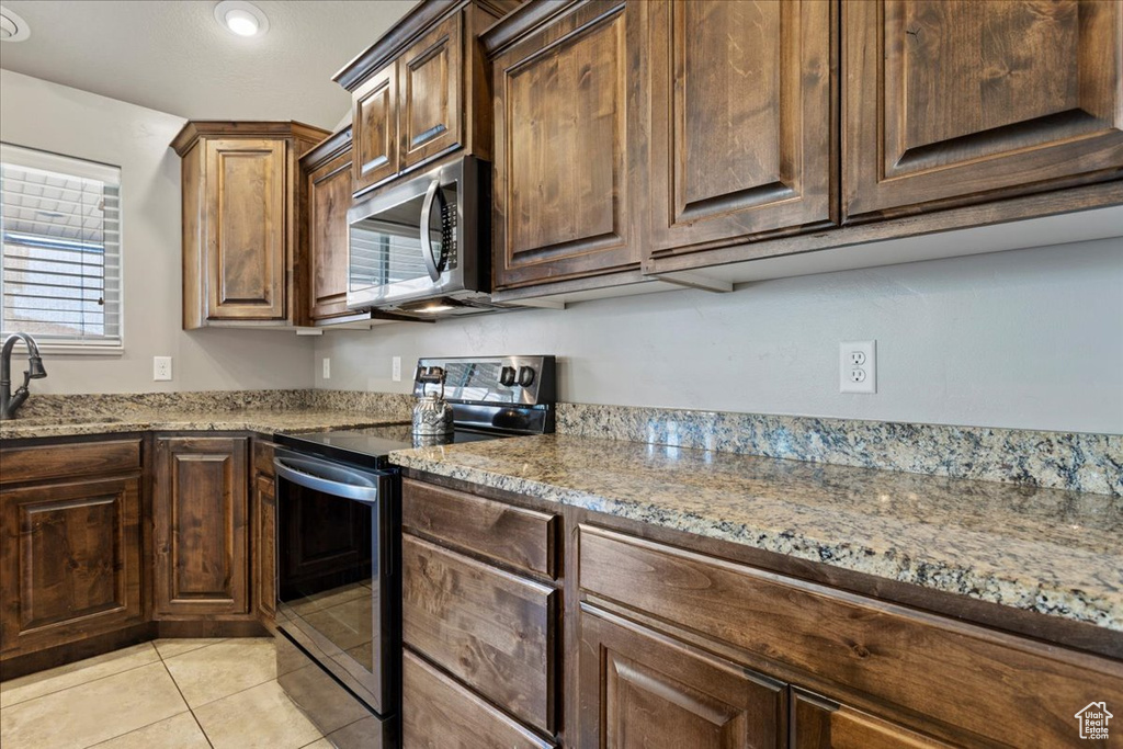 Kitchen with light stone counters, sink, electric range, and light tile floors