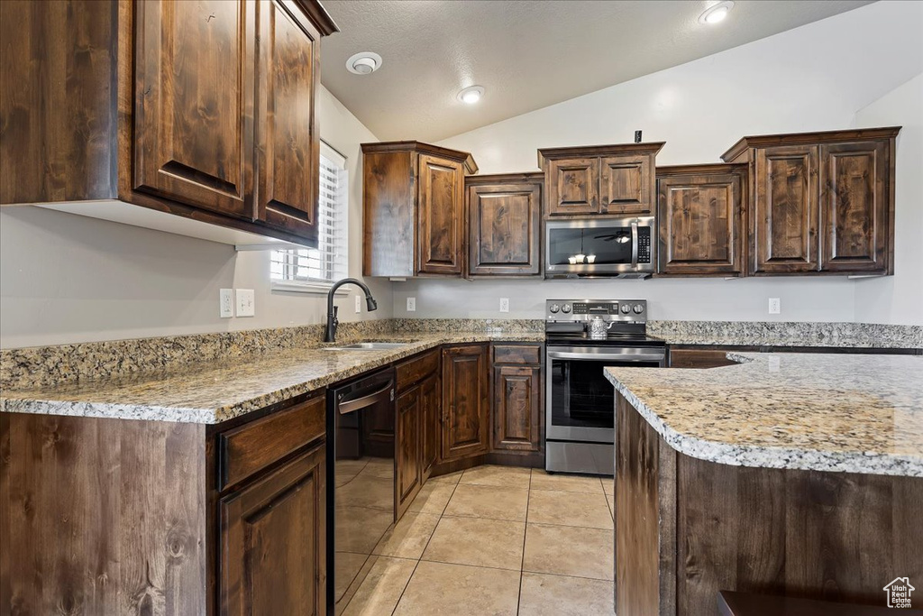 Kitchen featuring vaulted ceiling, dark brown cabinets, appliances with stainless steel finishes, sink, and light tile floors