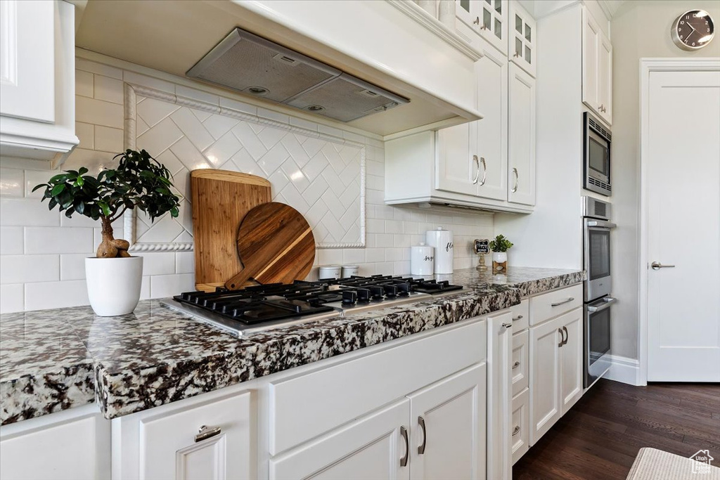 Kitchen featuring white cabinetry, appliances with stainless steel finishes, dark hardwood / wood-style floors, tasteful backsplash, and custom exhaust hood